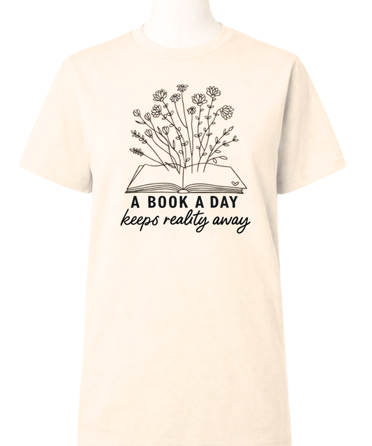 Beige t-shirt with a graphic of an open book with flowers and text 'A book a day keeps reality away' on a white background.