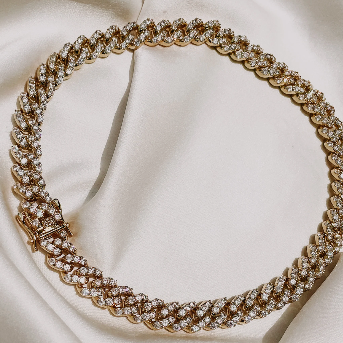 An 18K gold-plated brass necklace with cubic zirconia encrusted stones, displayed on a white fabric surface.