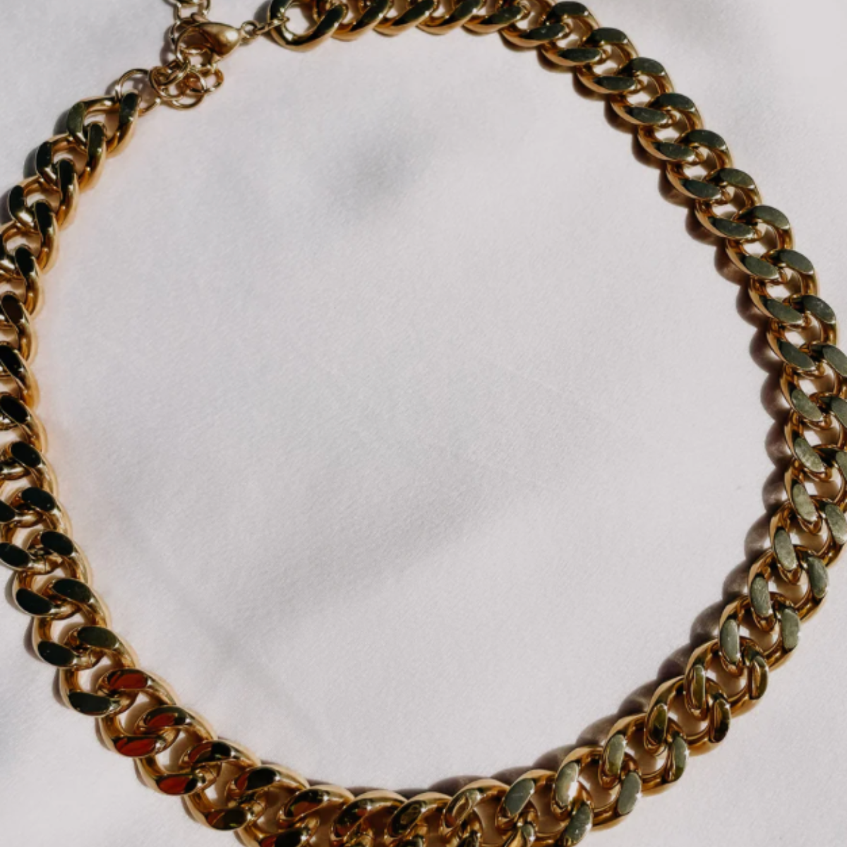 A gold-plated stainless steel chunky cuban chain necklace laid out on a white surface.
