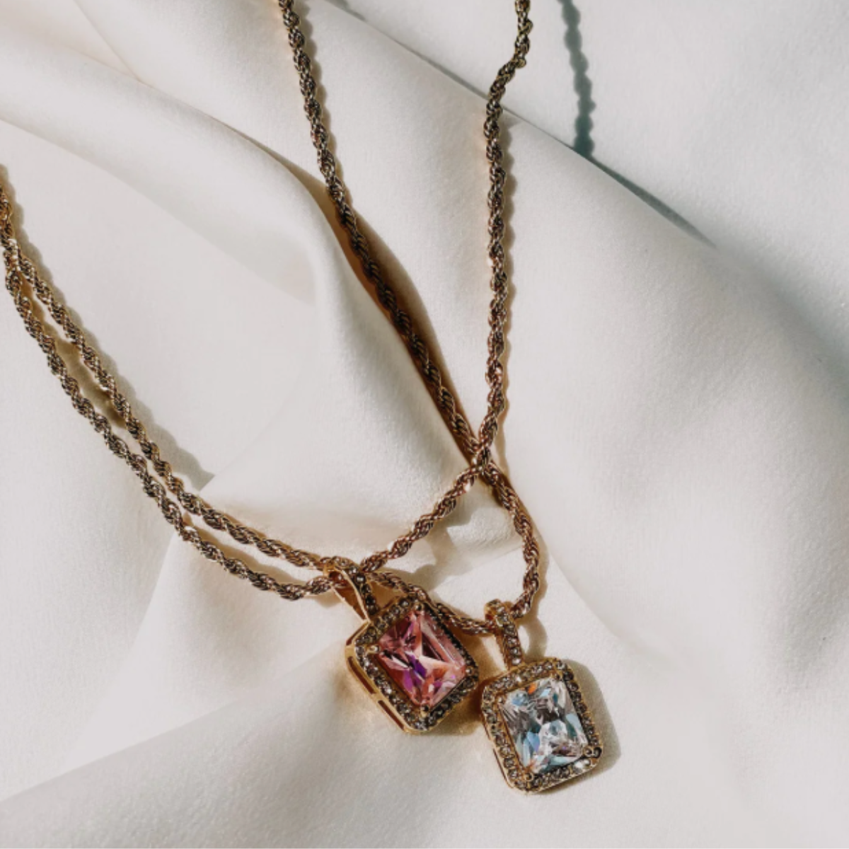 A gold-plated Kensington necklace with a rosé pendant on a white fabric background.