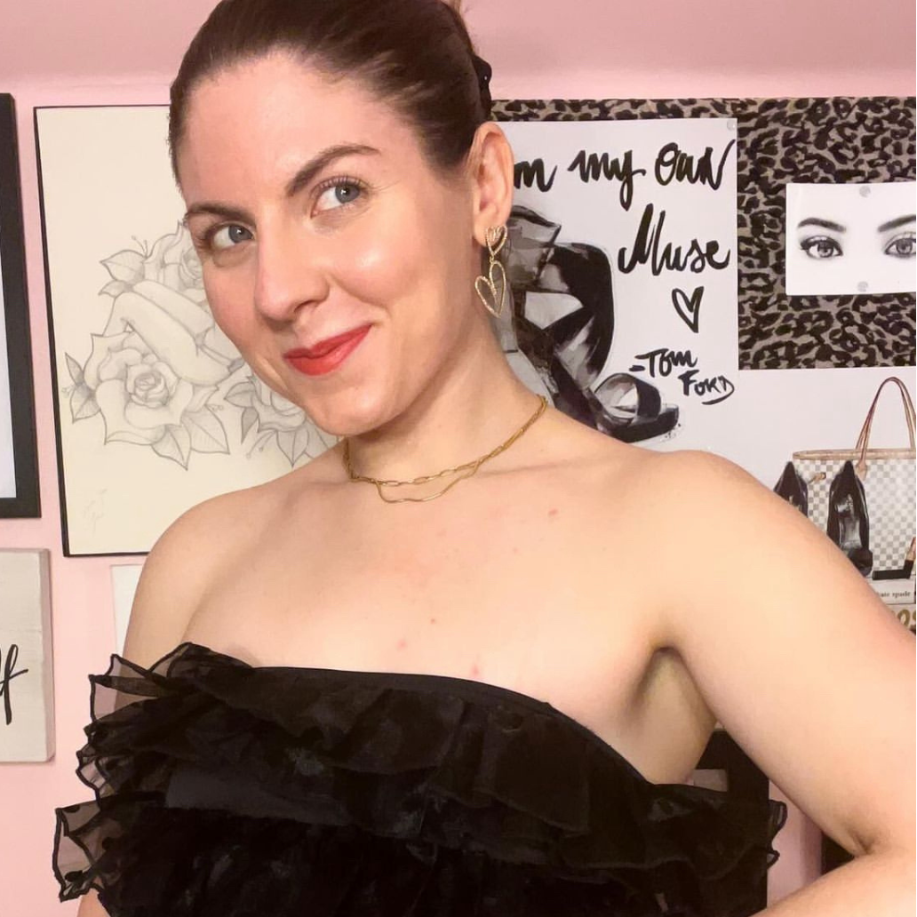 Woman wearing a black strapless top in front of a pink wall with artistic decorations.