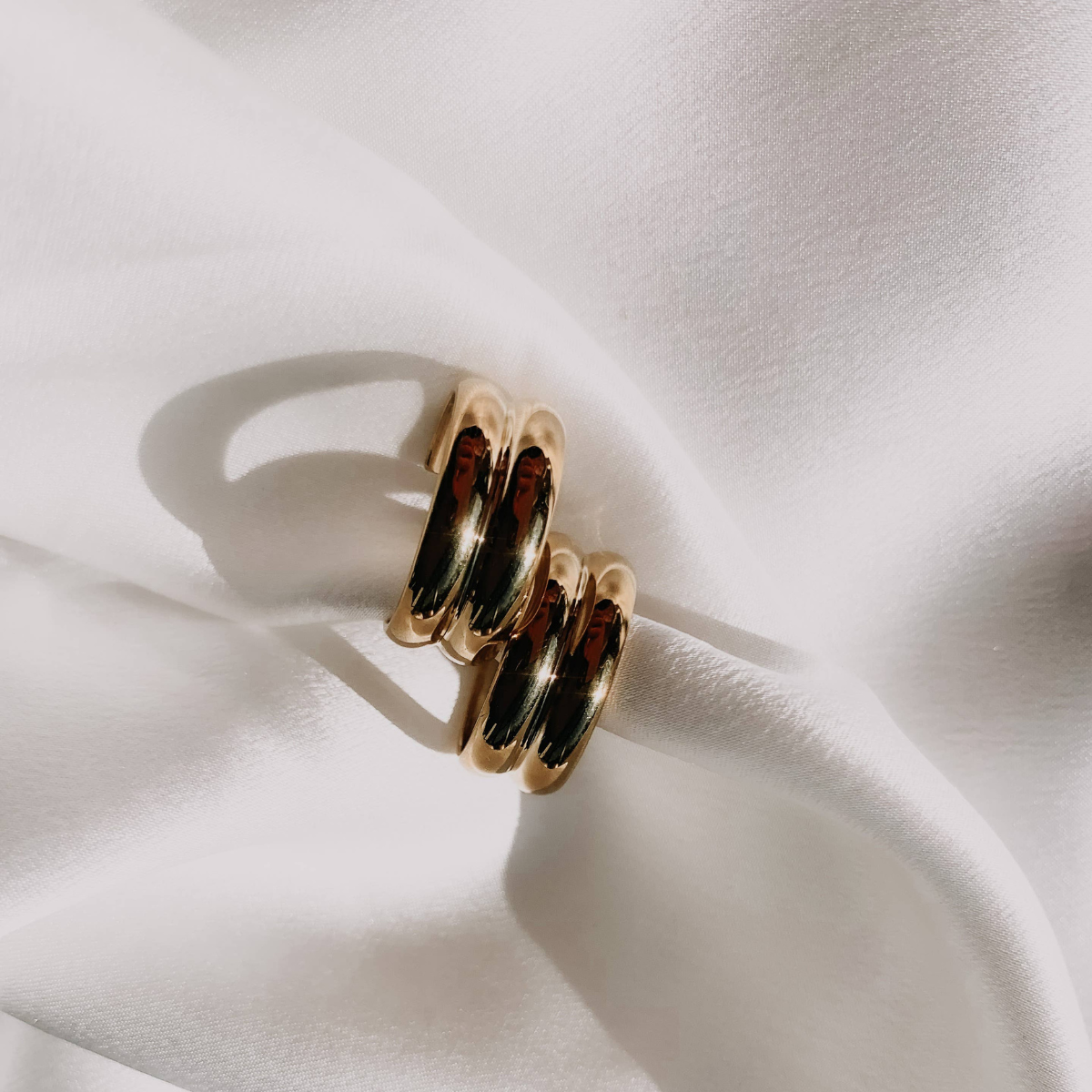 A close-up image of a gold-plated brass hoop earring on a white fabric background.