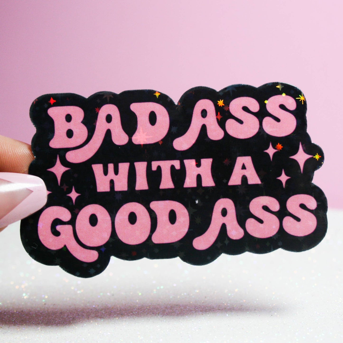 A sticker with pink and black colors, featuring the text 'BADASS WITH A GOOD ASS' in a handwritten-style font.