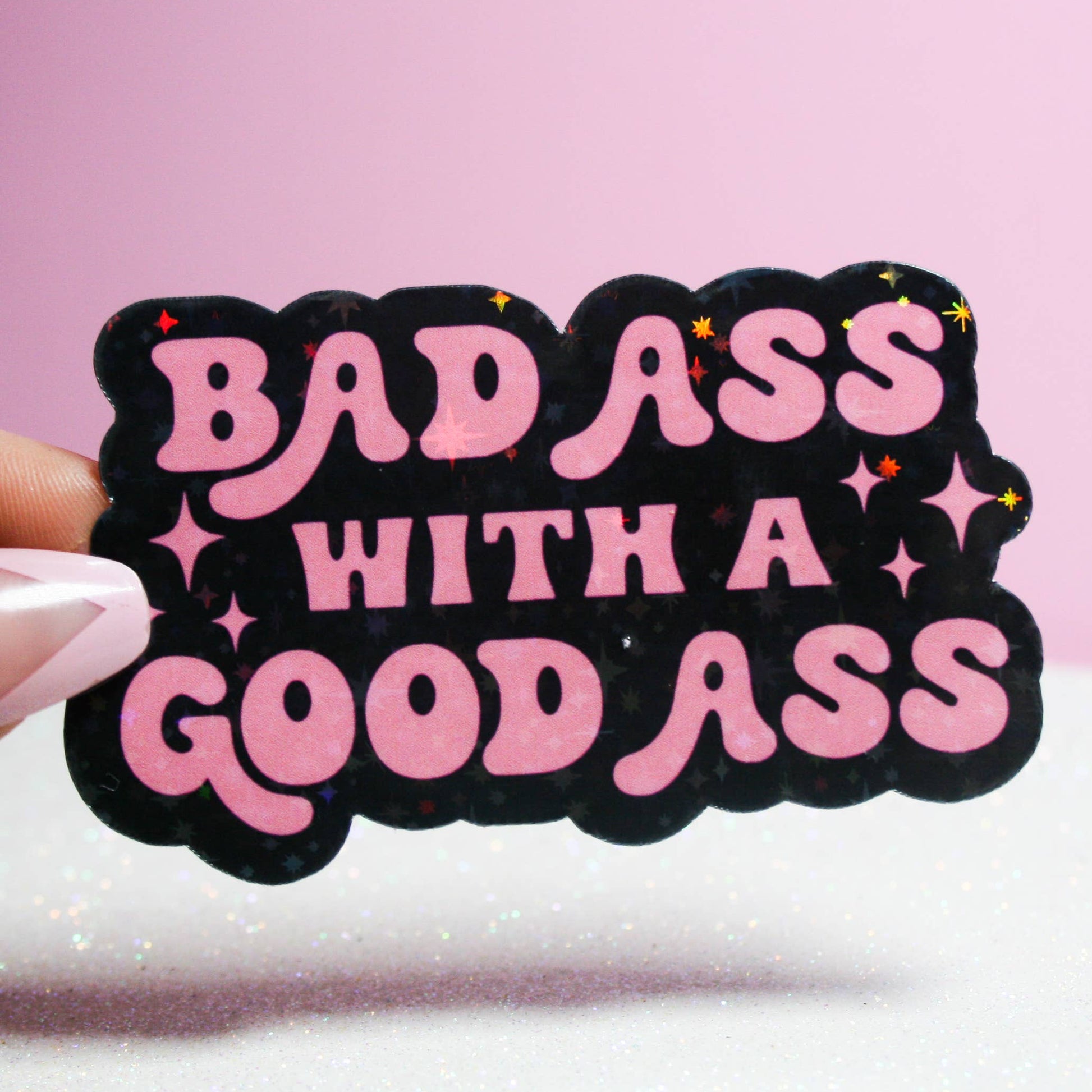 A sticker with pink and black colors, featuring the text 'BADASS WITH A GOOD ASS' in a handwritten-style font.