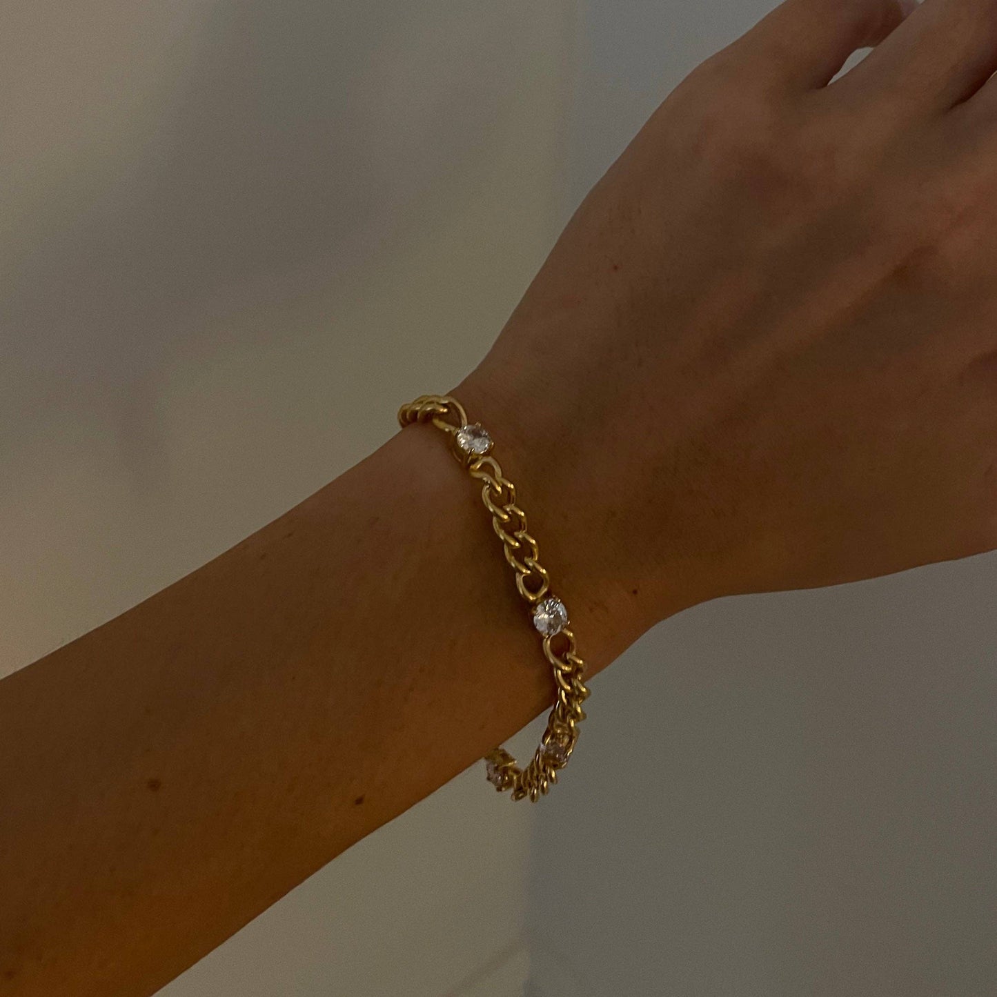 Gold bracelet on a wrist with a plain background