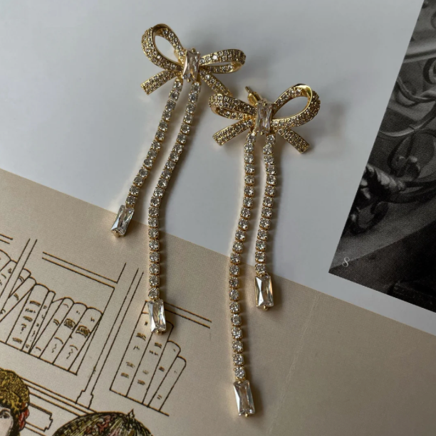Gold bow-shaped earrings with rhinestones on a vintage-style background