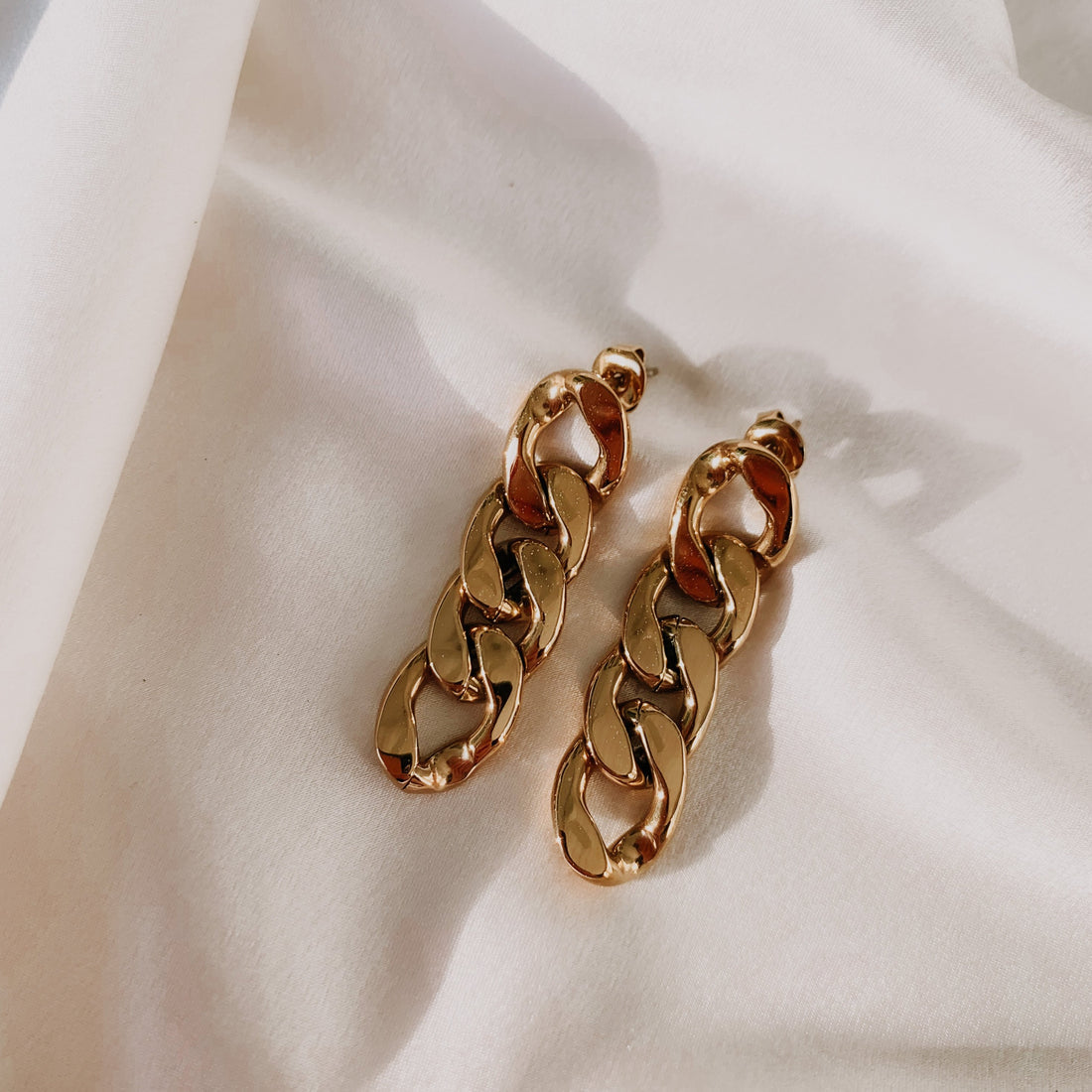 A pair of gold-colored rum and cigar earrings with a classic cuban chain design laid out on a white surface.